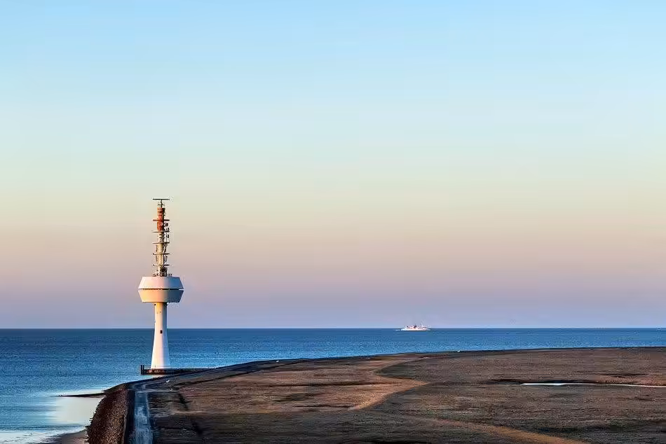 The Radar Tower On Neuwerk With A View Of The Elbe. In The Background The Helgoland Ferry Is Sailing.