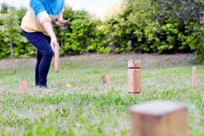 A Woman Deftly Throws A Kubb Throwing Stick Onto The Playing Field.