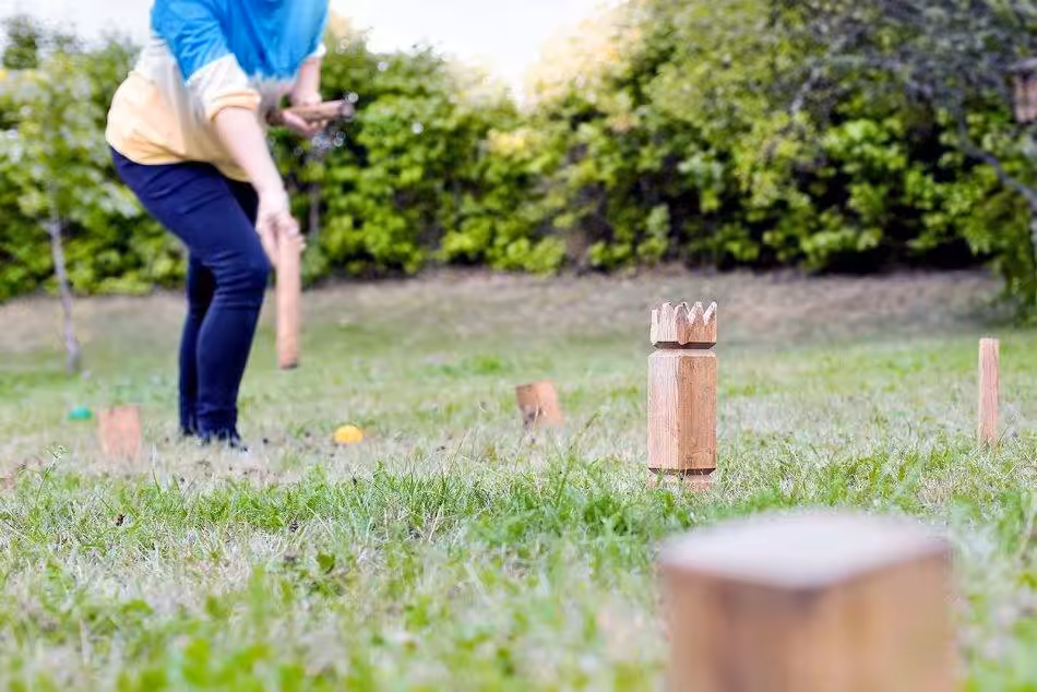 A Woman Deftly Throws A Kubb Throwing Stick Onto The Playing Field.